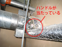 建築設備定期検査現場写真。防火ダンパーのハンドルが配管に当たって閉まらない